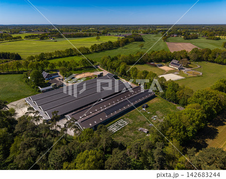 High angle wide horizontal aerial drone photograph of commercial livestock barns, rooftop solar panels, feed silos, and pastures in rural Gelderland, Achterhoek, Netherlands on sunny spring day High angle wide horizontal aerial drone photograph of commercial livestock barns, rooftop solar panels, feed silos, and pastures in rural Gelderland, Achterhoek, Netherlands on sunny spring day 142683244