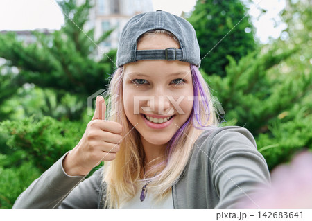 Teenage girl taking selfie showing thumbs up gesture outdoors close up Teenage girl taking selfie showing thumbs up gesture outdoors close up 142683641