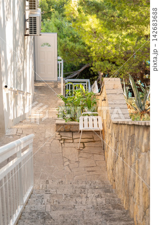 Sunlit stone staircase beside white house and lush garden greenery 142683688