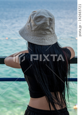 Back View of Young Woman Wearing Bucket Hat by Seaside Back View of Young Woman Wearing Bucket Hat by Seaside 142683721