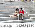 Fashionable African American student friends talking beside laptop on wide urban steps downtown 142684330