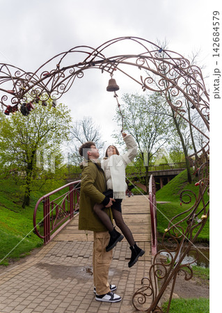 Smiling young man lifts his girlfriend beneath an ornate iron arch Smiling young man lifts his girlfriend beneath an ornate iron arch 142684579