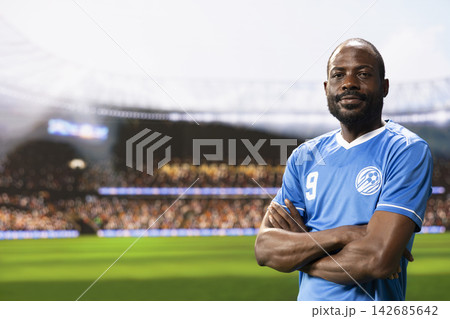 Portrait of african american player with arms crossed posing on pitch, stadium entrance before football game. Athlete in blue jersey creates copy space scene, sportsman on match day. Portrait of african american player with arms crossed posing on pitch, stadium entrance before football game. Athlete in blue jersey creates copy space scene, sportsman on match day. 142685642