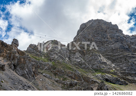 Rocky Mountain Cliff with Cable Cars and Dramatic Cloudy Sky 142686082