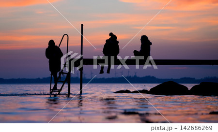 People Silhouettes on Lake Pier at Colorful Sunset People Silhouettes on Lake Pier at Colorful Sunset 142686269