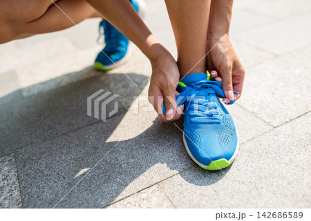 Runner Tying Blue Running Shoes on Sunny Pavement Runner Tying Blue Running Shoes on Sunny Pavement 142686589