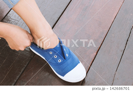 Blue Canvas Sneaker on Foot Over Wooden Floor Blue Canvas Sneaker on Foot Over Wooden Floor 142686701