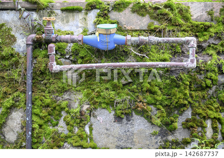 An old pipe with a faucet on a moss-covered wall 142687737