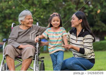 affectionate grandmother gently stroking granddaughter head while family looks on in park 142688509