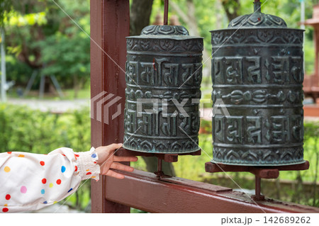 Cropped shot view of woman hand try to spinning a prayer wheel in Tibetan Buddhist monastery. Prayer wheels are devices for spreading spiritual blessings and well being. Cropped shot view of woman hand try to spinning a prayer wheel in Tibetan Buddhist monastery. Prayer wheels are devices for spreading spiritual blessings and well being. 142689262