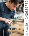 Skillful woodworker carving old layers from wooden board with chisel tool in restoration workshop. 142689789