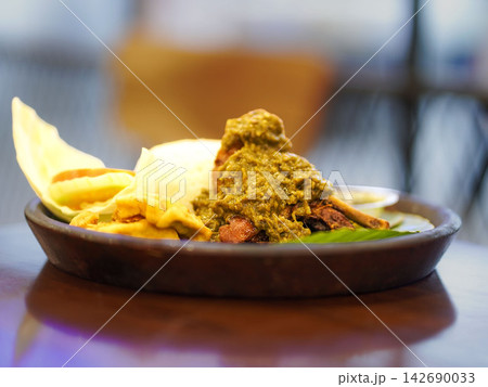Traditional Indonesian duck dish (bebek sambal ijo) topped with rich green chili sambal, served alongside steamed white rice, fried tofu, tempeh, and fresh cucumber garnish on a traditional banana lea Traditional Indonesian duck dish (bebek sambal ijo) topped with rich green chili sambal, served alongside steamed white rice, fried tofu, tempeh, and fresh cucumber garnish on a traditional banana lea 142690033