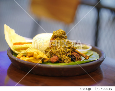 Traditional Indonesian duck dish (bebek sambal ijo) topped with rich green chili sambal, served alongside steamed white rice, fried tofu, tempeh, and fresh cucumber garnish on a traditional banana lea 142690035