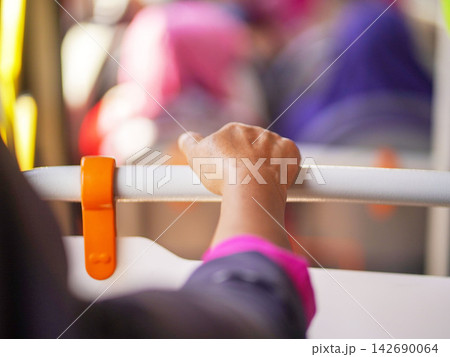 Close-up of a passenger's hand holding a handrail handle inside a public transport bus or train for balance during a daily city commute. Close-up of a passenger's hand holding a handrail handle inside a public transport bus or train for balance during a daily city commute. 142690064