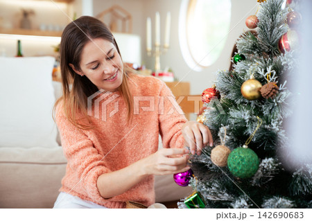 Caucasian woman decorating Christmas tree with ornaments at home Caucasian woman decorating Christmas tree with ornaments at home 142690683