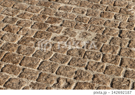 Close-up view of weathered cobblestone pavement showing square stones, sandy joints Close-up view of weathered cobblestone pavement showing square stones, sandy joints 142692187