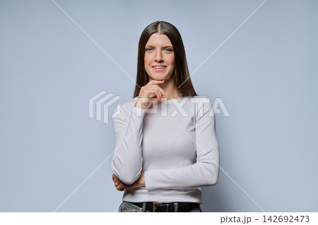 Portrait of thoughtful young woman holding hand on chin on grey background 142692473