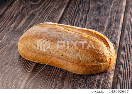 Freshly baked golden brown loaf of bread on dark rustic wooden table, crusty texture and flour dusting visible Freshly baked golden brown loaf of bread on dark rustic wooden table, crusty texture and flour dusting visible 142692667