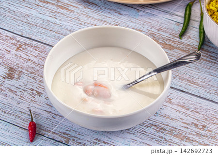 Creamy prawn soup in white bowl with spoon, red and green chili peppers on rustic blue wooden table Creamy prawn soup in white bowl with spoon, red and green chili peppers on rustic blue wooden table 142692723