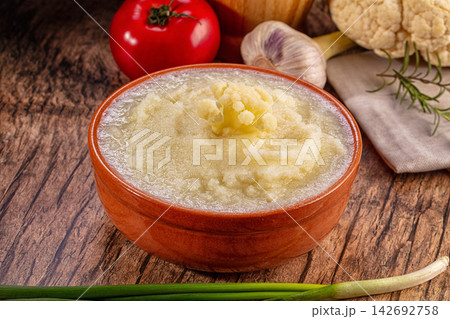 Homemade cauliflower puree in a rustic clay bowl surrounded by fresh vegetables on a wooden table Homemade cauliflower puree in a rustic clay bowl surrounded by fresh vegetables on a wooden table 142692758