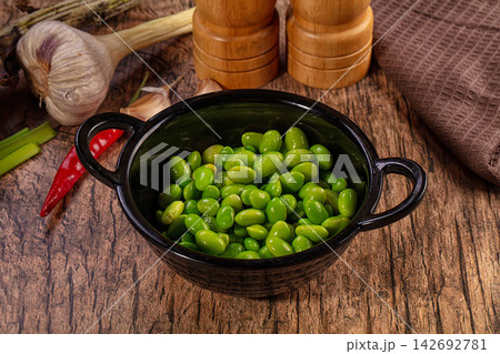 Fresh green edamame beans in black ceramic bowl on rustic wooden table with garlic, red chili and wooden salt and pepper grinders Fresh green edamame beans in black ceramic bowl on rustic wooden table with garlic, red chili and wooden salt and pepper grinders 142692781