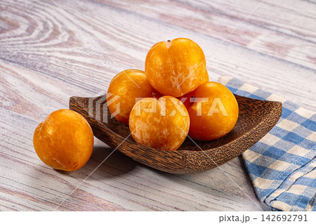 Yellow plums in rustic wooden bowl on weathered wood table with blue and white checkered cloth beside Yellow plums in rustic wooden bowl on weathered wood table with blue and white checkered cloth beside 142692791