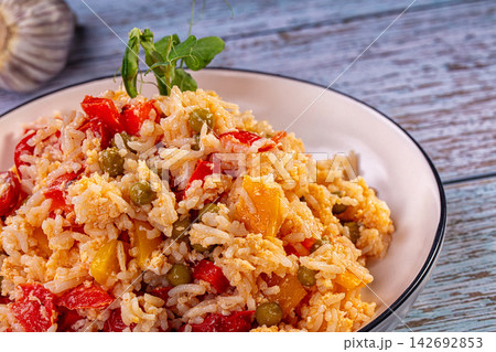 Fried basmati rice with red bell peppers, green peas, and yellow squash served in white bowl on rustic blue wooden table Fried basmati rice with red bell peppers, green peas, and yellow squash served in white bowl on rustic blue wooden table 142692853