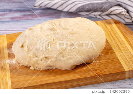 Homemade yeast dough for bread or pizza resting on rustic bamboo cutting board, light flour coating, vibrant blue and purple background Homemade yeast dough for bread or pizza resting on rustic bamboo cutting board, light flour coating, vibrant blue and purple background 142692890