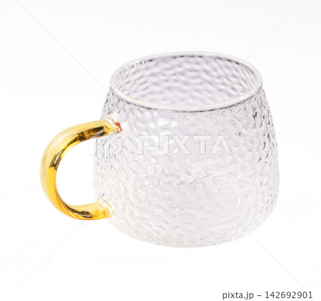 Clear textured glass mug with golden handle on white background, shallow depth of field, modern minimalist style Clear textured glass mug with golden handle on white background, shallow depth of field, modern minimalist style 142692901