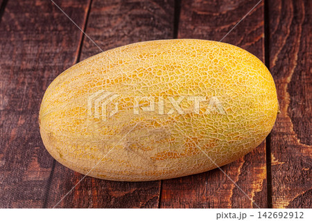 Ripe cantaloupe melon with netted rind resting on dark rustic wooden surface, warm natural lighting highlighting texture and golden yellow tones Ripe cantaloupe melon with netted rind resting on dark rustic wooden surface, warm natural lighting highlighting texture and golden yellow tones 142692912