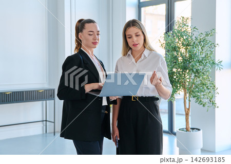 Two business women looking at laptop screen working together in bright office 142693185