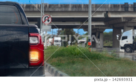 Dark pickup truck stopped beneath an urban highway bridge during a daytime commute.Car surface is wet with raindrops. Road surface is wet from rain. Truck is moving past. Blurred of No U turn sign. Dark pickup truck stopped beneath an urban highway bridge during a daytime commute.Car surface is wet with raindrops. Road surface is wet from rain. Truck is moving past. Blurred of No U turn sign. 142693931