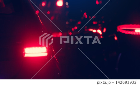 Abstract rear view of a vehicle with glowing red tail lights driving on a dark street at night. Scene of heavy traffic at night shrouded in darkness with only the glow of vehicle taillights visible. Abstract rear view of a vehicle with glowing red tail lights driving on a dark street at night. Scene of heavy traffic at night shrouded in darkness with only the glow of vehicle taillights visible. 142693932