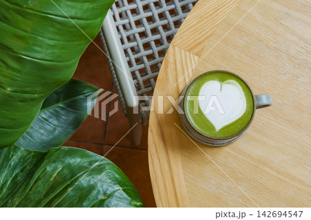 sweet hot matcha latte art in heart shape put on wooden table with green leaf plant decoration in conner sweet hot matcha latte art in heart shape put on wooden table with green leaf plant decoration in conner 142694547