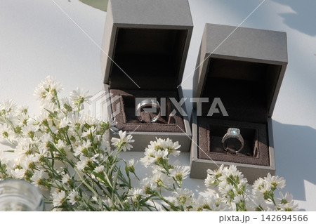 The wedding rings are in boxes on a corner of a white table, decorated with dried flowers The wedding rings are in boxes on a corner of a white table, decorated with dried flowers 142694566