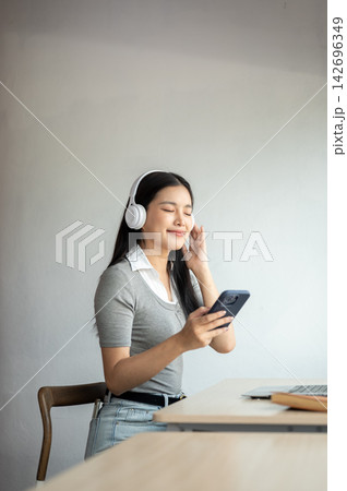Young Asian woman closing eyes listening to music in headphones while sitting at table in a cafe. Young Asian woman closing eyes listening to music in headphones while sitting at table in a cafe. 142696349