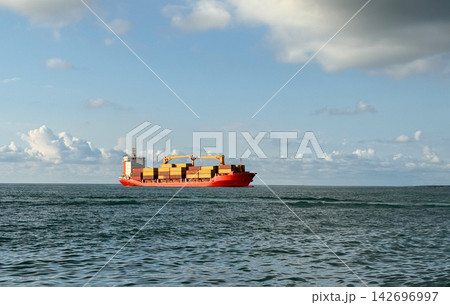 A large container ship sails on the ocean water under a blue sky. The ship is filled  142696997