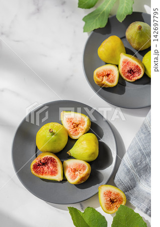 Fresh Ripe Figs with Green Leaves on a Two Plates on a Marble Background 142697795