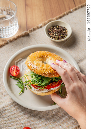 Hand holding a fresh bagel with prosciutto tomato, cheese and lettuce. Hand holding a fresh bagel with prosciutto tomato, cheese and lettuce. 142697799