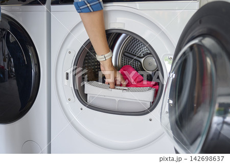 Hand pulling lint filter from open tumble dryer with clothes inside drum Hand pulling lint filter from open tumble dryer with clothes inside drum 142698637
