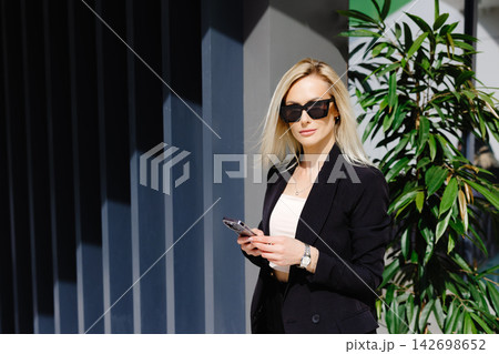 Young businesswomen in black suit using smartphone isolated on background gray wall. Pretty manager holding mobile gadget and texting message 142698652