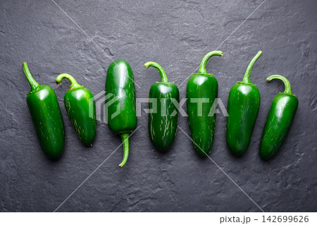 Row of jalapeno peppers on dark stone background Row of jalapeno peppers on dark stone background 142699626