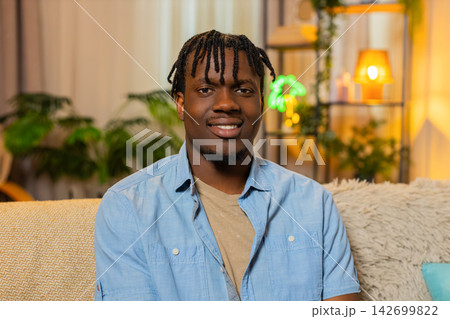 African American young man on home sofa changes serious expression to calm smile for portrait shot 142699822