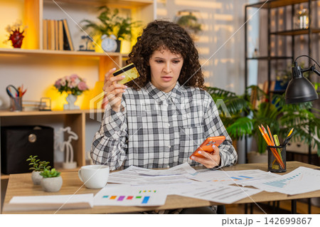 Young woman on home table checking bills on smartphone and planning home budget with careful concern 142699867