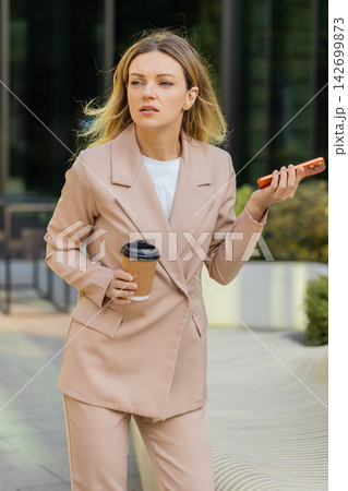 Young woman calling late business partner walking in city street with takeaway coffee before meeting Young woman calling late business partner walking in city street with takeaway coffee before meeting 142699873