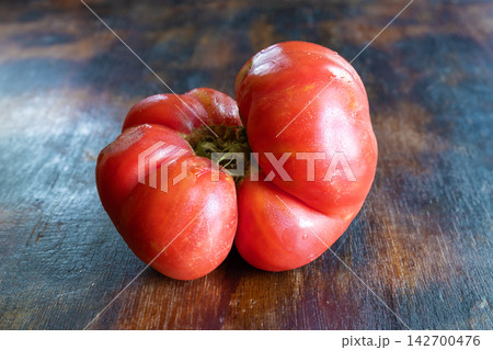 Close-up of ugly, naturally misshapen tomato with unusual irregular form and multiple lobes, on rustic wooden surface. The ripe red vegetable shows natural variations in shape and texture Close-up of ugly, naturally misshapen tomato with unusual irregular form and multiple lobes, on rustic wooden surface. The ripe red vegetable shows natural variations in shape and texture 142700476