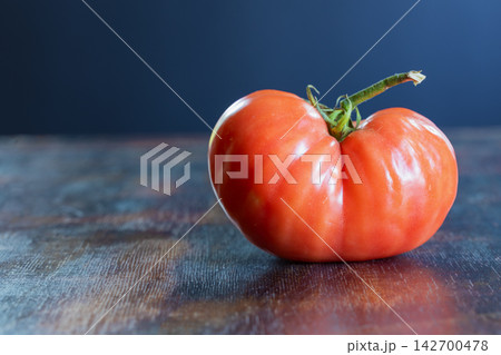 Close-up of ugly, naturally misshapen tomato with unusual irregular shape and pronounced lobes, resting on rustic wooden surface. Concept of accepting imperfect food, agricultural diversity Close-up of ugly, naturally misshapen tomato with unusual irregular shape and pronounced lobes, resting on rustic wooden surface. Concept of accepting imperfect food, agricultural diversity 142700478