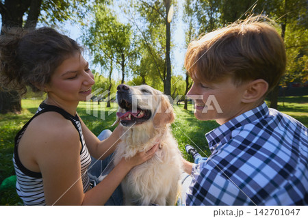 Golden retriever smiles between affectionate young couple in close portrait Golden retriever smiles between affectionate young couple in close portrait 142701047