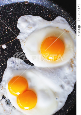 Two sunny-side up eggs frying in a nonstick pan Two sunny-side up eggs frying in a nonstick pan 142702371