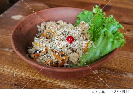 A bowl of rice salad displayed on a wooden table in a rustic interior creates a feeling of freshness and health. A bowl of rice salad displayed on a wooden table in a rustic interior creates a feeling of freshness and health. 142703919